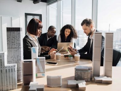 Hospitality professionals sitting around a conference table with architectural building models, discussing a project in a modern office.
