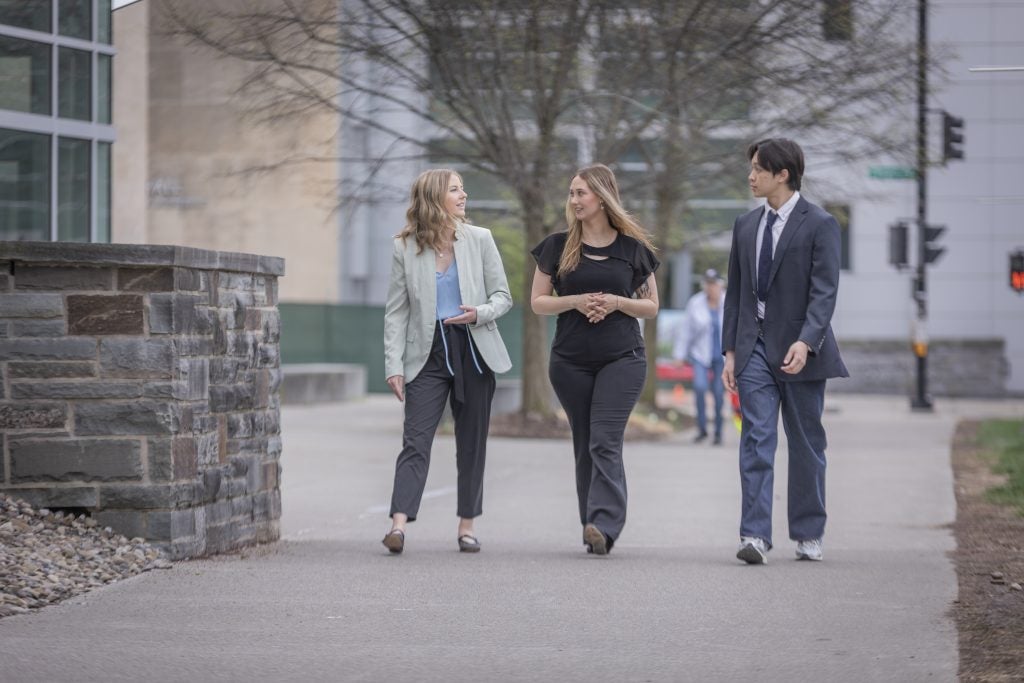 Three Cornell MMH students walking in front of Statler Hall engaged in conversation. 