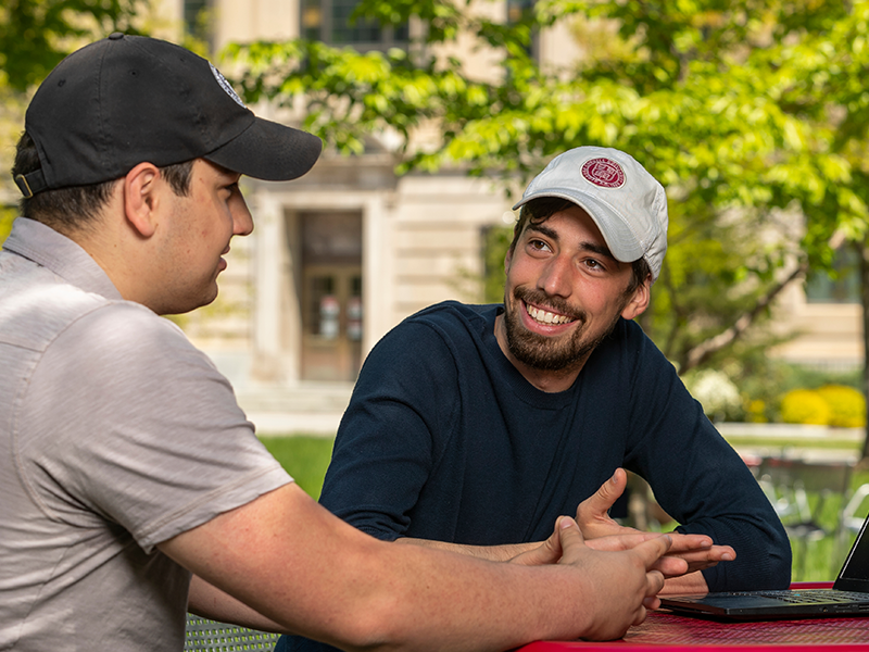 Two MPS AEM students in front of Warren hall having a discussion in front of a laptop.