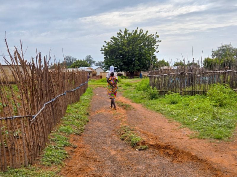 A woman carrying a child walk down a dirt path in Ghana.