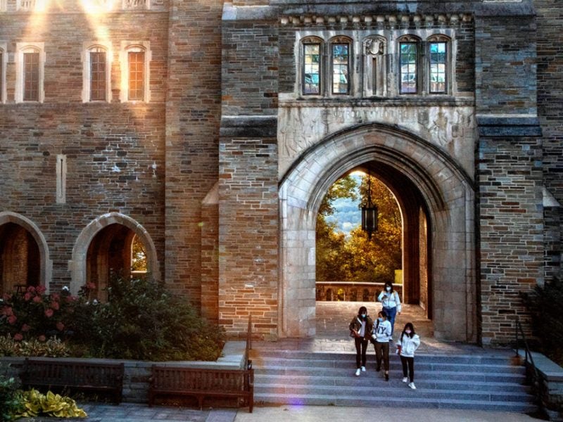 Students sitting on the steps of the Cornell Law School with the sun setting just behind the stone-and-mortar building