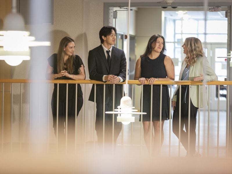 Cornell MMH students leaning on banister in Statler Hall, having a discussion.