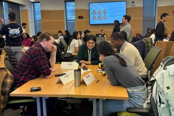 Two women students and two men students collaborate at a table within a populated open classroom as part of the Cornell MBA immersive curriculum