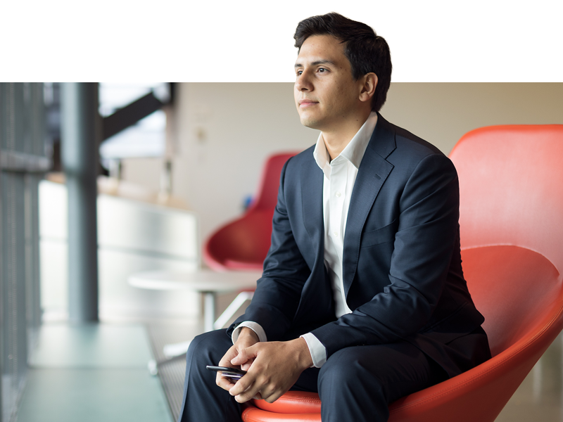 Male student in a red chair gazing out pensively in a suit.