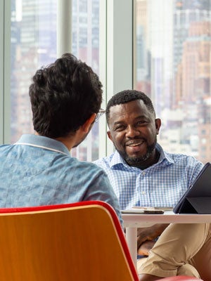Two business analytics students having a one-on-one discussion in a campus meeting room with a city skyline in the background.