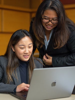 Two 1-B students smile while looking at a laptop screen together