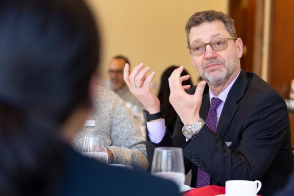 A man in a suit speaks over a table to someone
