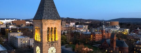 McGraw Tower, a tall stone and steel clock tower in the center of Cornell University's campus in Ithaca, New York, in the evening with the belfry alit