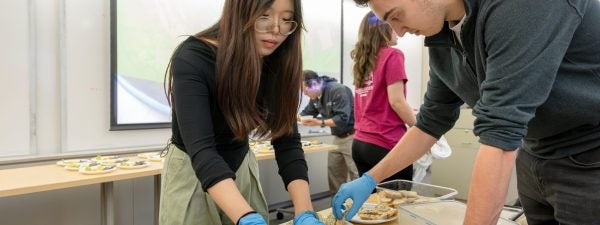 Two students lean over a table to assemble plates of food.