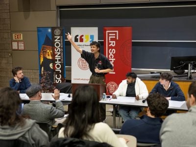 Student speaking at a podium raises his hand to emphasize a point.