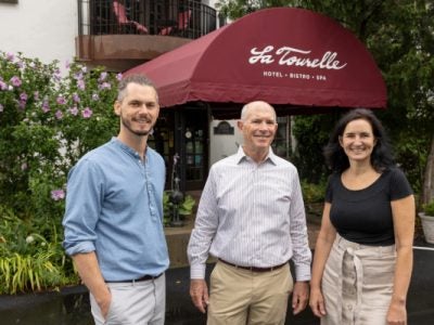 Bobby Frisch, Bill Minnock, and Lisa Chervinsky stand in front of the hotel entrance with the maroon La Tourelle awning behind them.