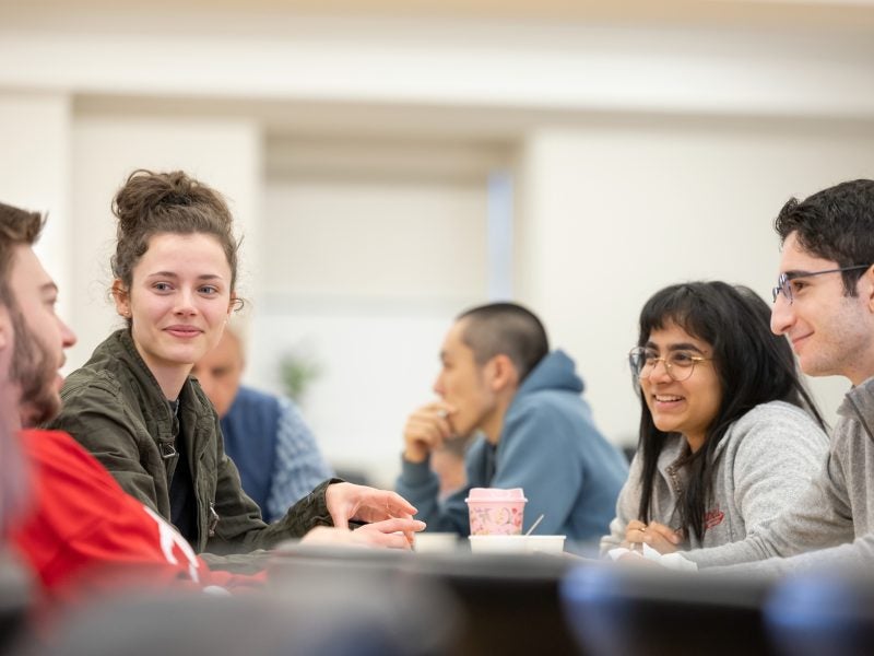 Several CEMS Master in International Management students sit at a table and discuss a project while smiling