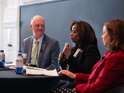Image of a man and two women sitting at a table with a microphone