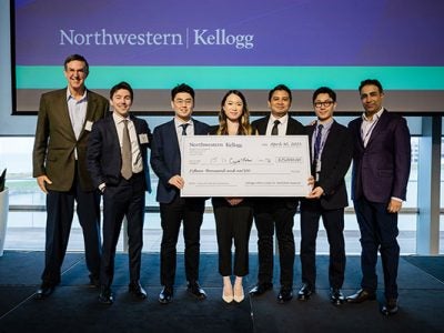 One older man standing next to 6 students in business attire holding novelty check for $15,000.
