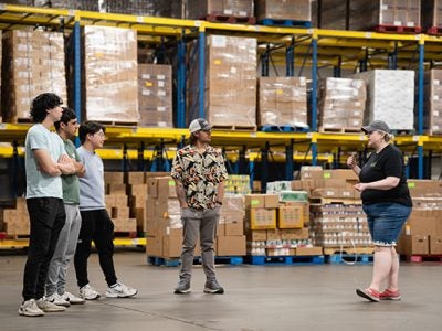 Image of four male students listening to a volunteer in a warehouse.