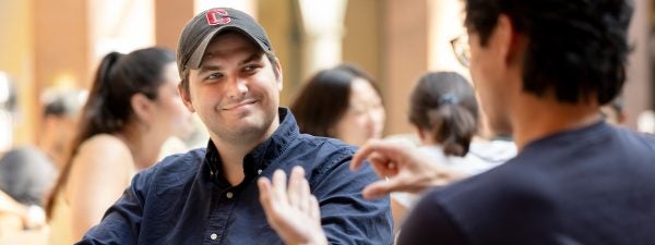 MBA student in Dyson Atrium with Cornell baseball cap on engaging with other student