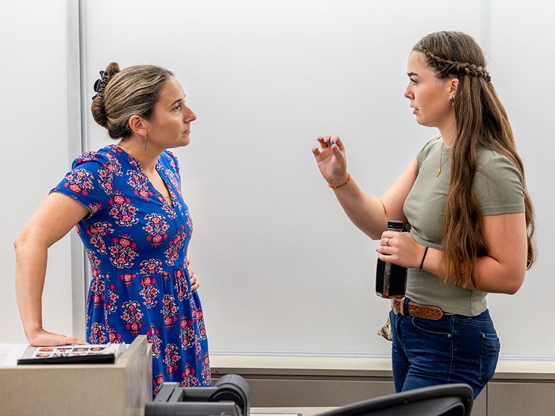 A student talking to a faculty member in front of a white board in a classroom.