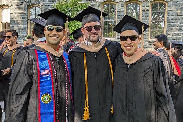 3 men in graduation caps and gowns on Cornell&rsquo;s Arts Quad.