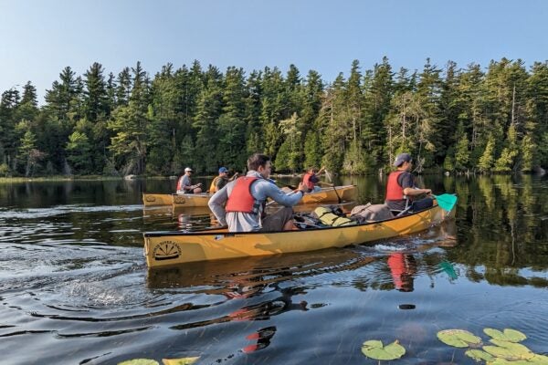 Cornell MBA students row in a yellow canoe in a calm lake against a mountainous pine tree setting