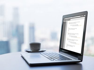 a laptop sitting on a desk with a coffee cup next to it, blurred buildings in the background.