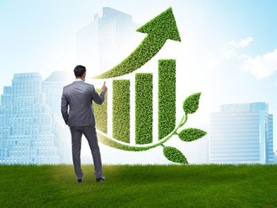 Green economy growth concept with businessman standing in front of a rising bar chart made of green foliage