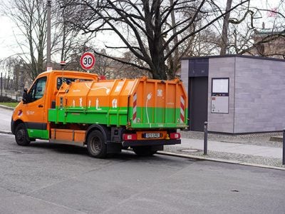 orange and green electric garbage truck with electric cord graphic on the side