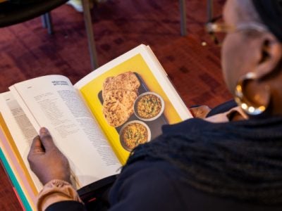A photo of a woman looking at an open cookbook, taken from over her shoulder.