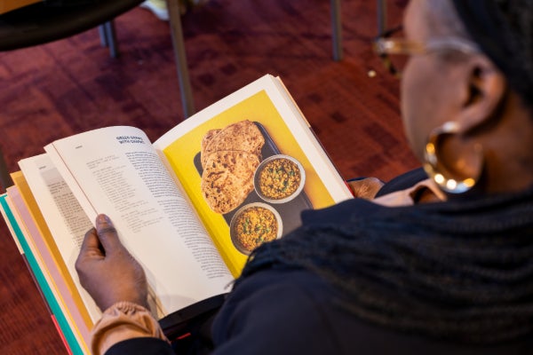 A photo of a woman looking at an open cookbook, taken from over her shoulder.
