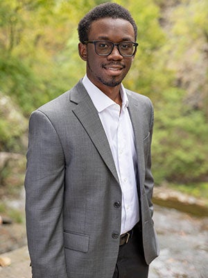 environemental photo of Albert Charles with greenery and a stone path in the background.