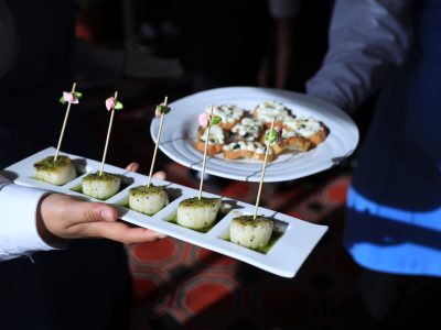 A close-up of two people carrying small portions of scallops and crostini.