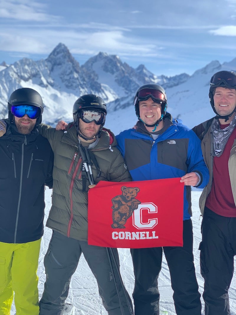 Four MBA students hold a Cornell banner in a posed photo at a ski resort.
