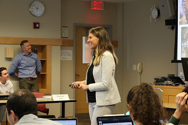 a young woman speaking to college students in a classroom.