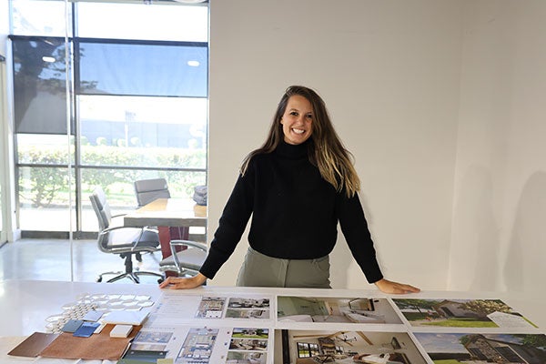 a young woman standing behind a large table displaying photos of interior designs.