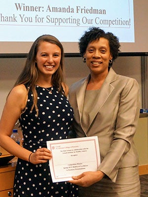 a young woman and older woman standing side be side, smiling and holding an awards certificate.