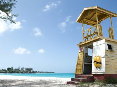 photo of a white sand beach and turquoise blue sea water with a wooden lifeguard station in the foreground.