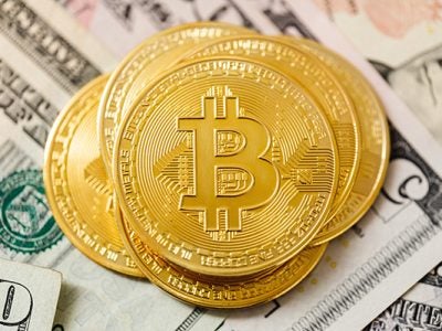 gold round Bitcoins sitting on dollar bills / paper currency