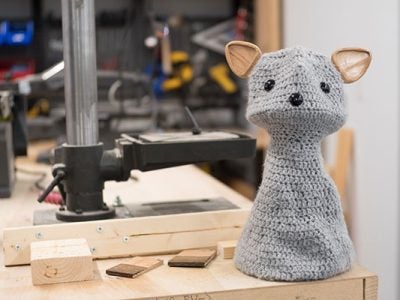 photo of a crocheted social robot that looks like a cat sitting in an engineering fabrication workshop