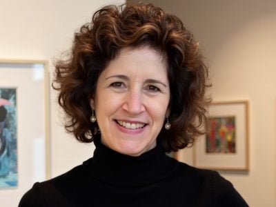 Headshot of a woman with brown curly hair standing in an art gallery.