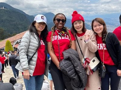 four women pose for a photo with tree-covered hilltips and sky on the background.