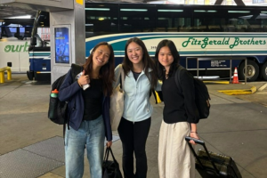 Three women standing with luggage in a bus station.