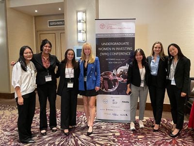 Woman students in business attire pose next to a WIN Conference banner.