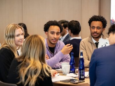 A student wearing purple speaks with other students at a table.
