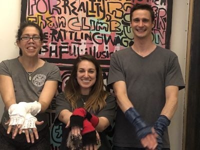 Austin, Alia, and Becki stand in front of colorful art and show their gloves