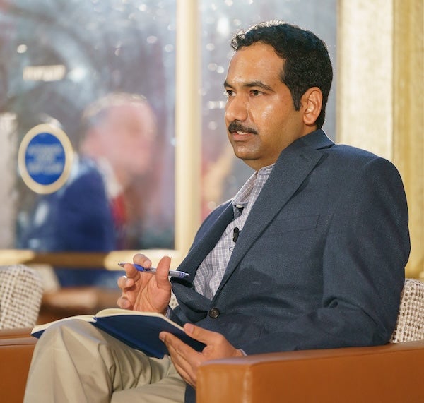 Mani Sethuraman sits in a chair on stage holding a notebook.