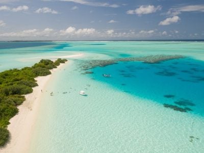 erial photo of a tropical island with a few anchored boats and people standing on the beach.