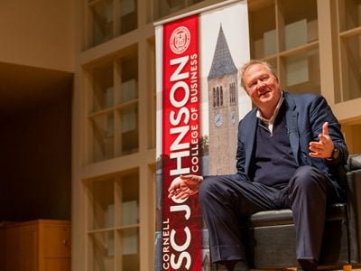 Jon Moeller sitting in a chair and speaking on stage with a SC Johnson College of Business banner in the background.