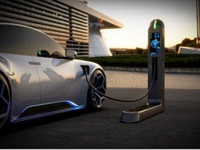photo of an electric vehicle plugged into an EV charging station next to an office building
