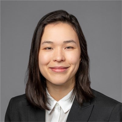 A young woman enrolled in the Cornell MBA program at the Johnson School smiles while in business casual attire on a gray background
