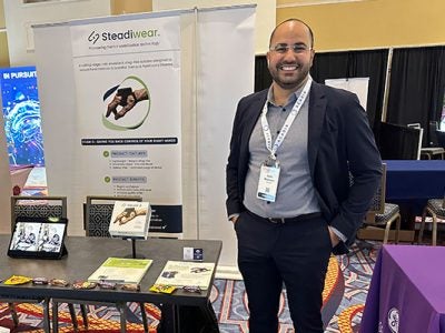 A man standing next to a table and a poster displaying information about Steadiwear.