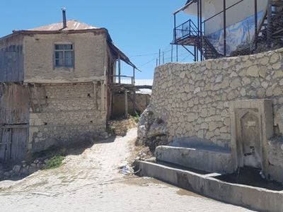 old, light grey stone building, wall, and road built on a steep incline.